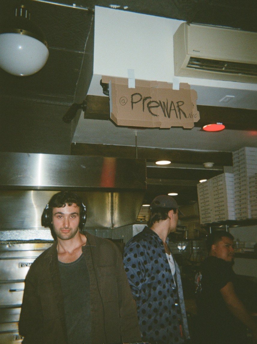 PREWAR under a cardboard @PREWAR sign in a pizza kitchen